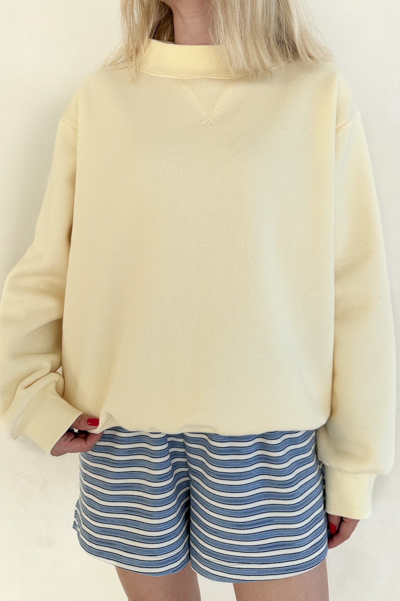 Person wearing a light yellow sweatshirt and blue striped shorts on a plain background