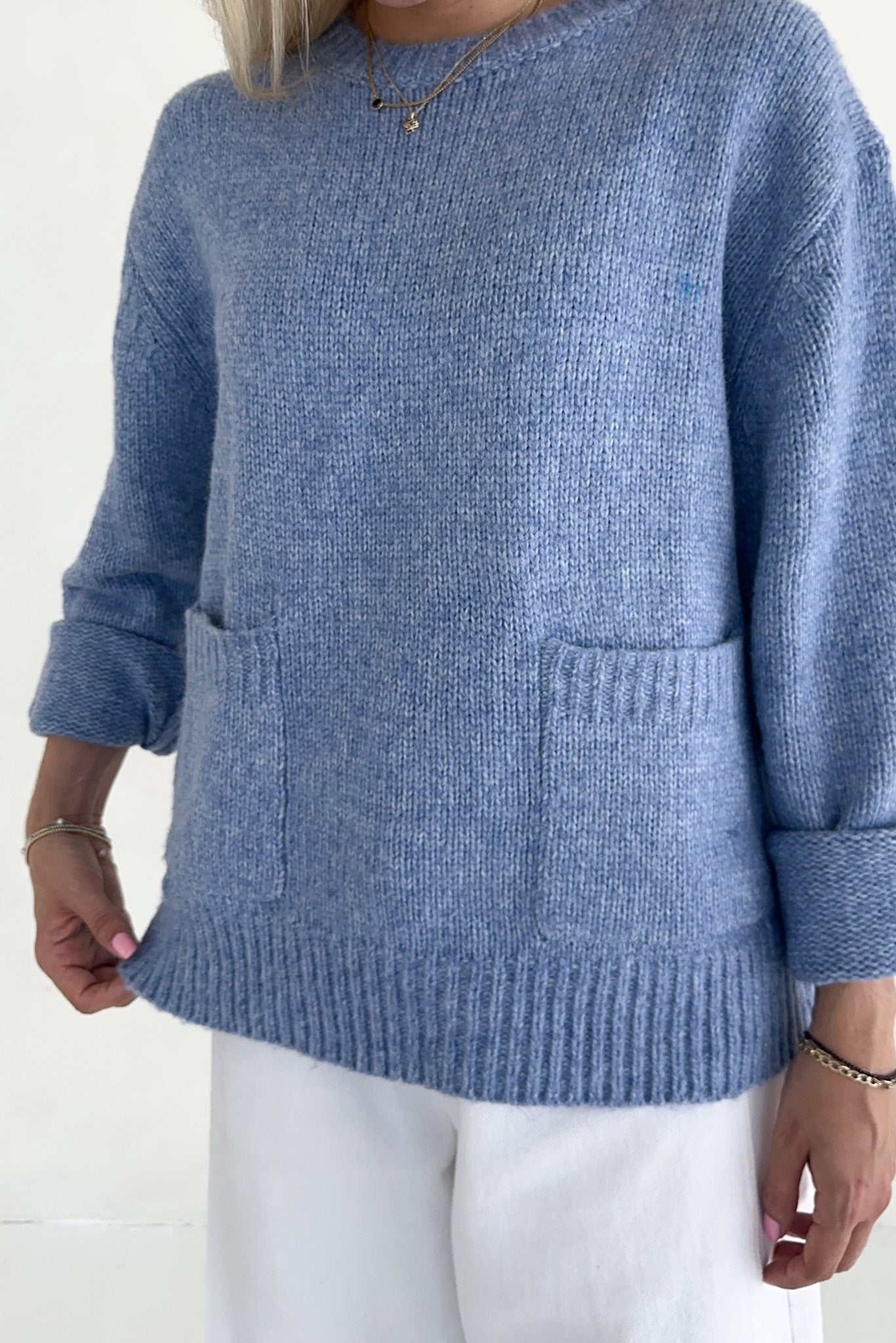 Blue knitted sweater worn by a person on a white background
