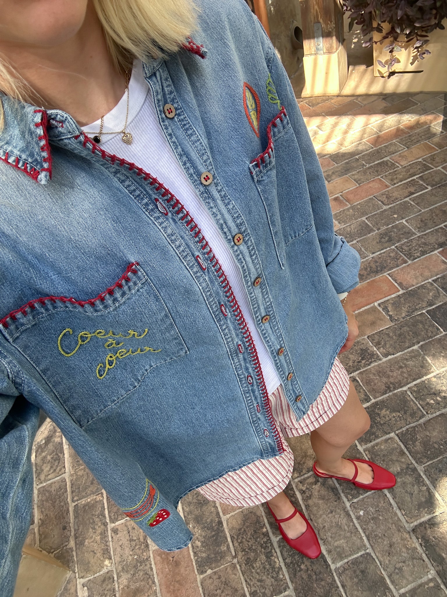 Person wearing a blue denim jacket with embroidery on a stone pavement