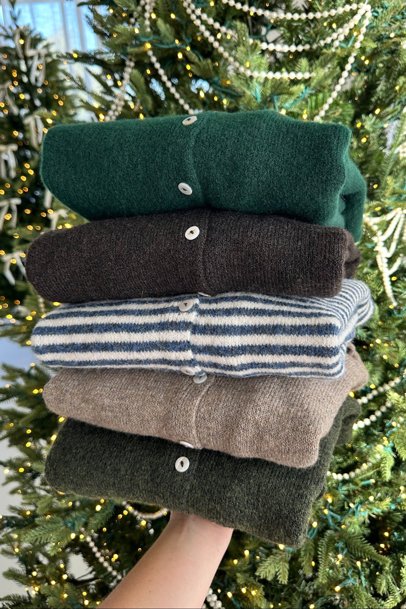 Stack of folded sweaters in front of a decorated Christmas tree