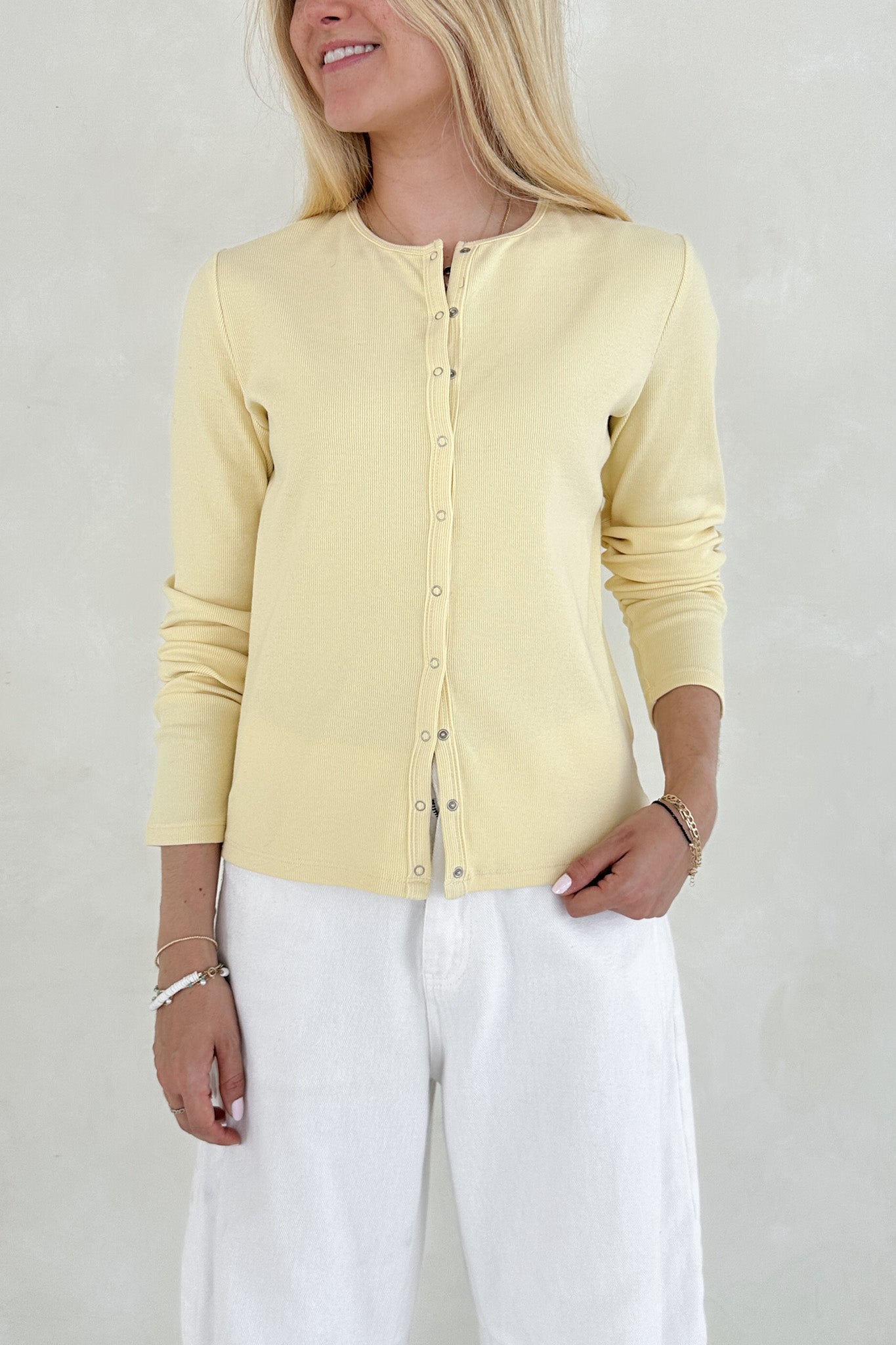 Woman wearing a light yellow cardigan over a white top with a neutral background