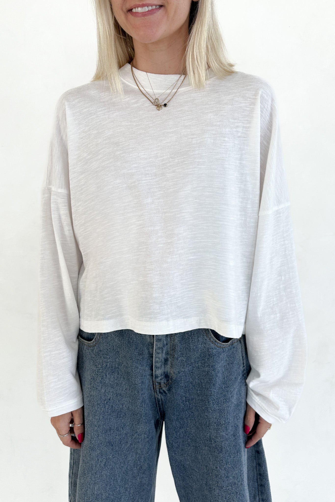 Person wearing a white long-sleeve top and blue jeans on a plain background