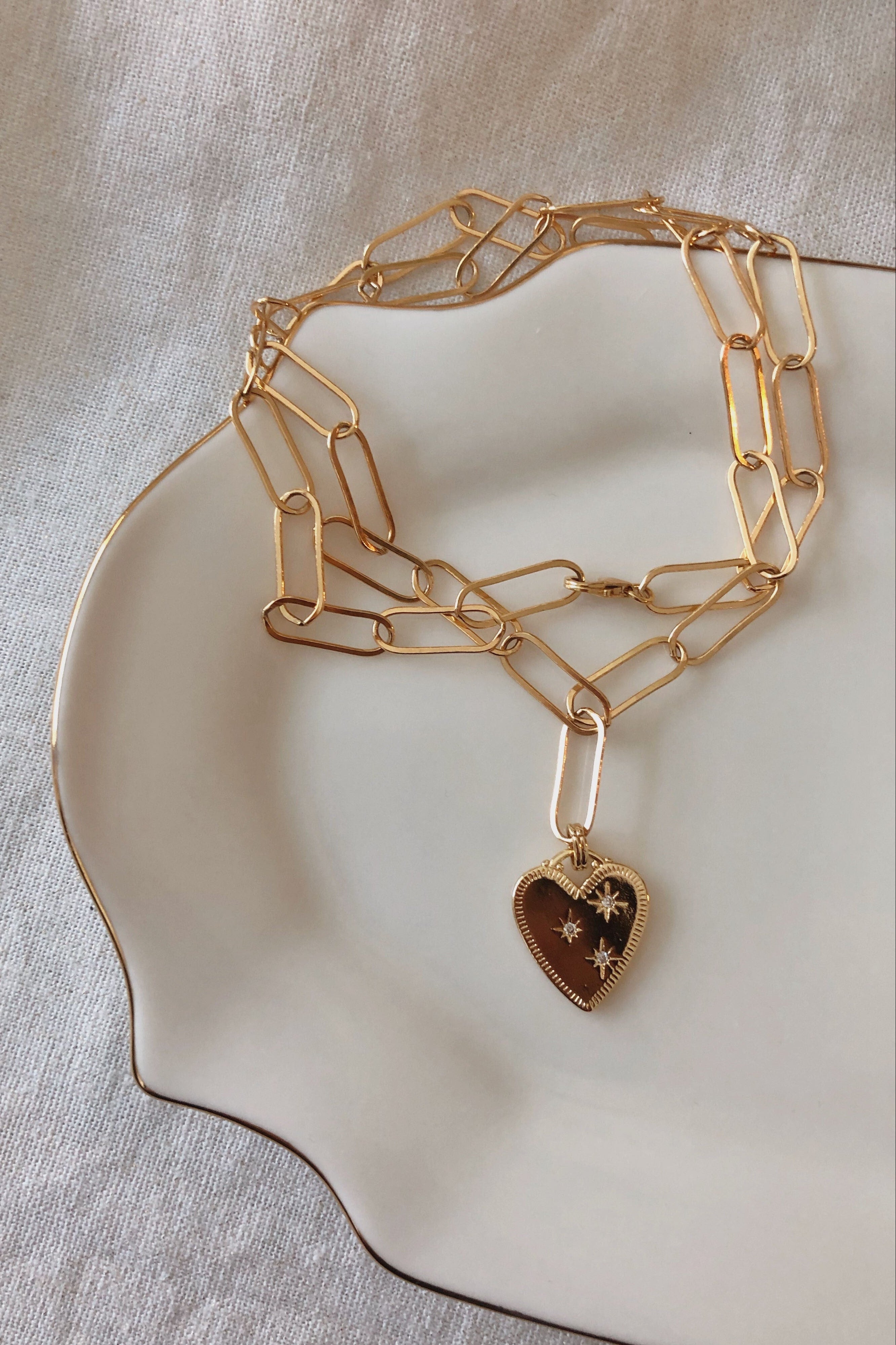 Gold chain necklace with a heart-shaped pendant on a beige dish.