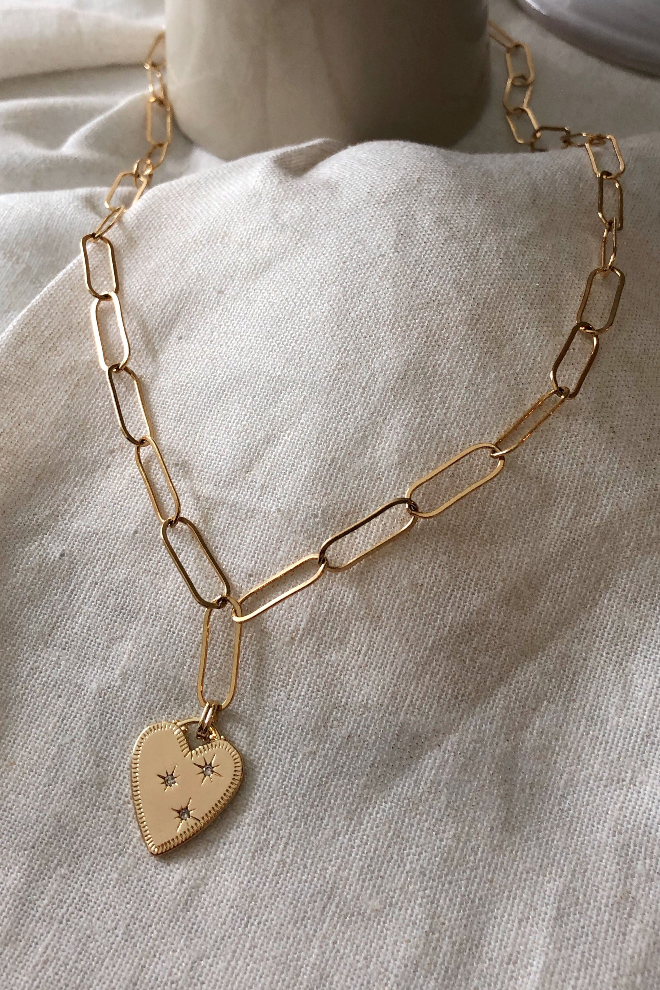 Gold chain necklace with a heart-shaped pendant on a light fabric background