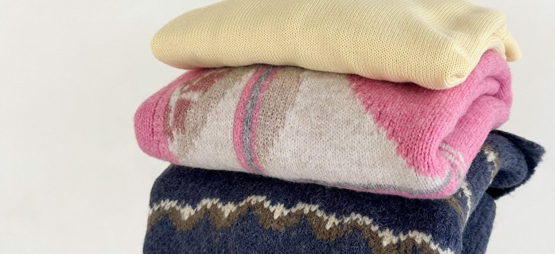 Stack of folded sweaters in yellow, pink, and blue on a white background