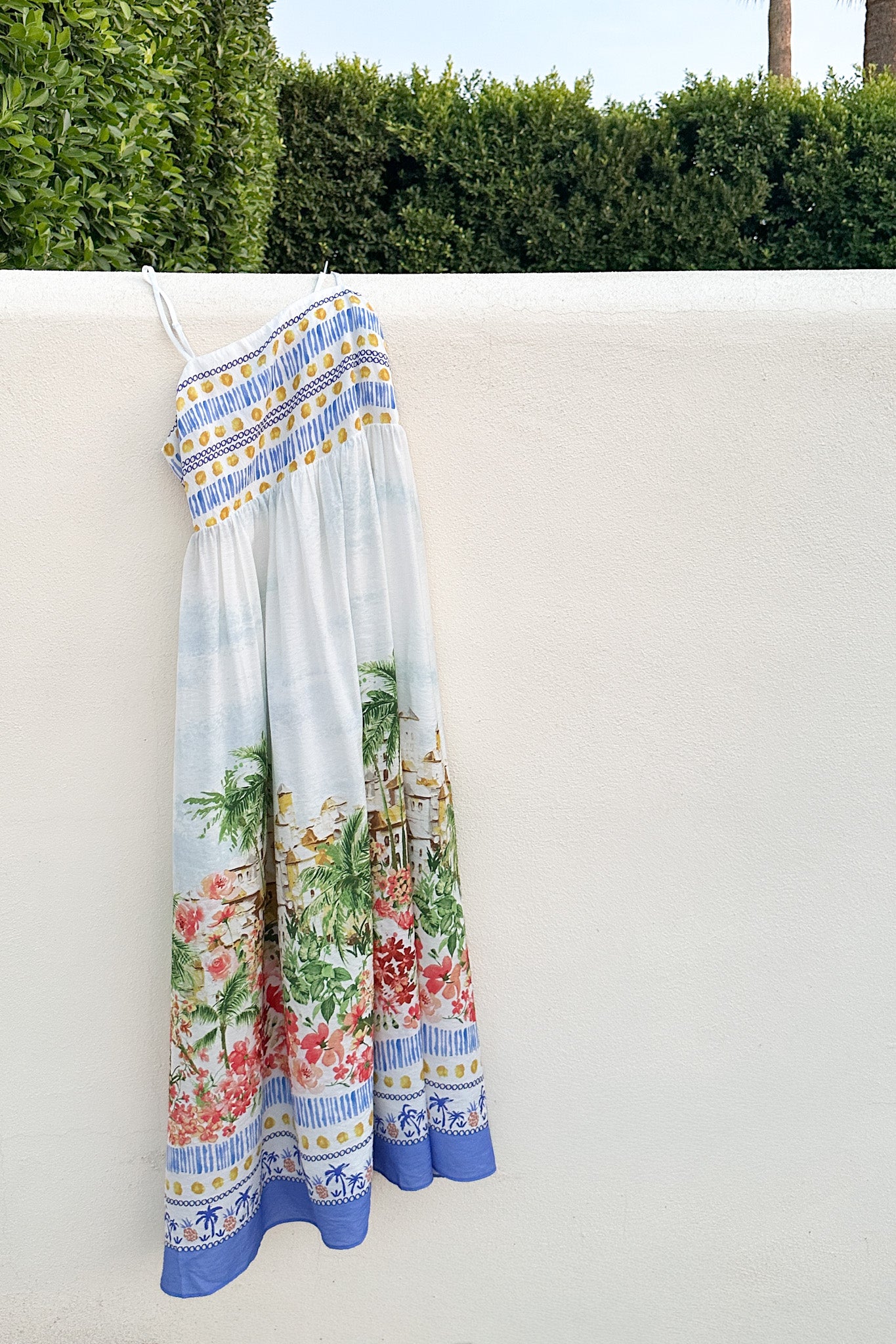 Colorful dress with floral design hanging on a white wall with greenery in the background