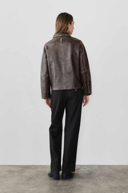 Person wearing a brown leather jacket and black pants against a white background