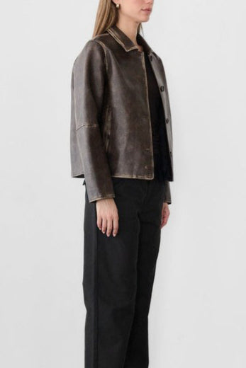 Woman wearing a brown leather jacket and black pants against a white background