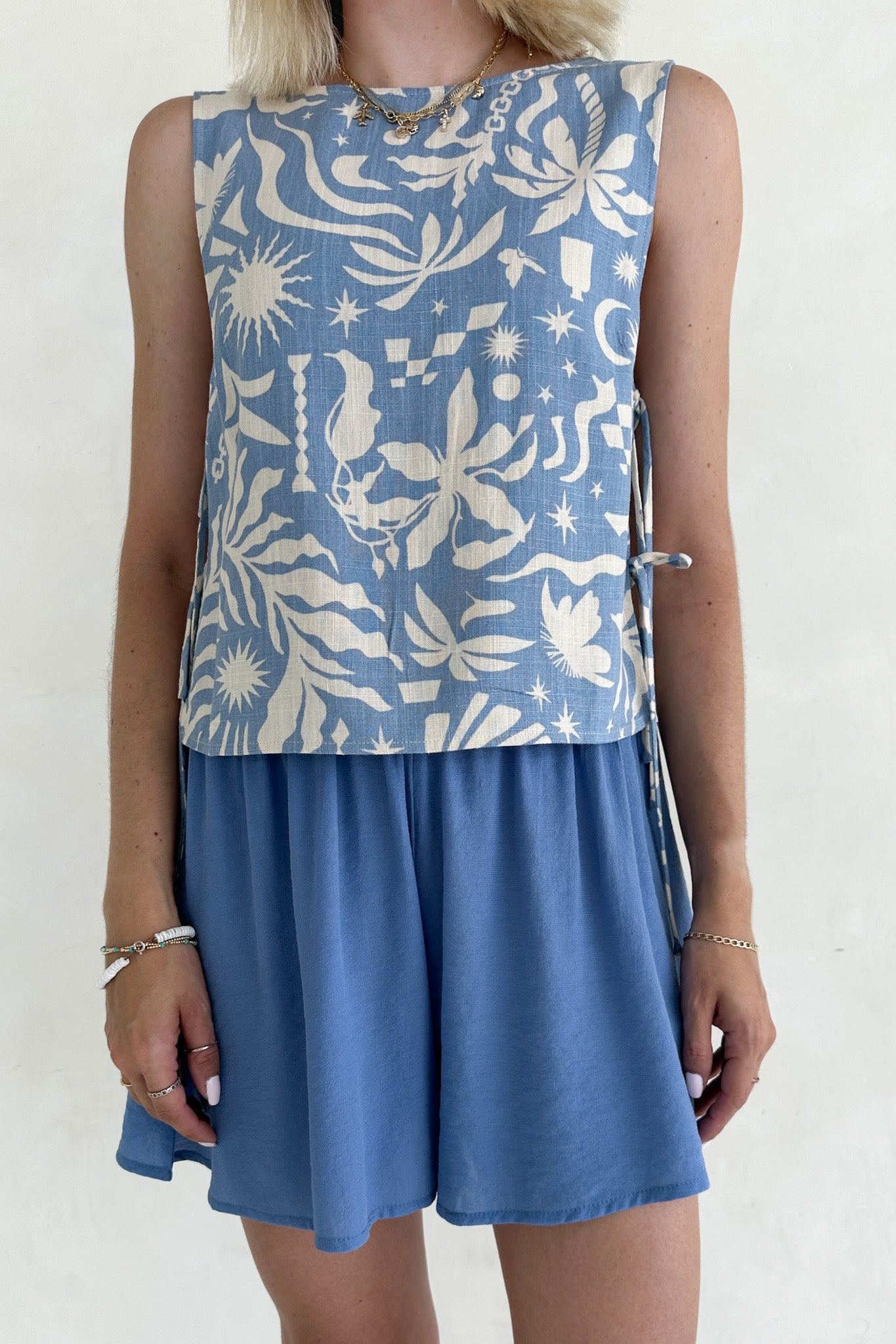 Woman wearing a blue sleeveless top with white floral pattern and matching skirt against a white background
