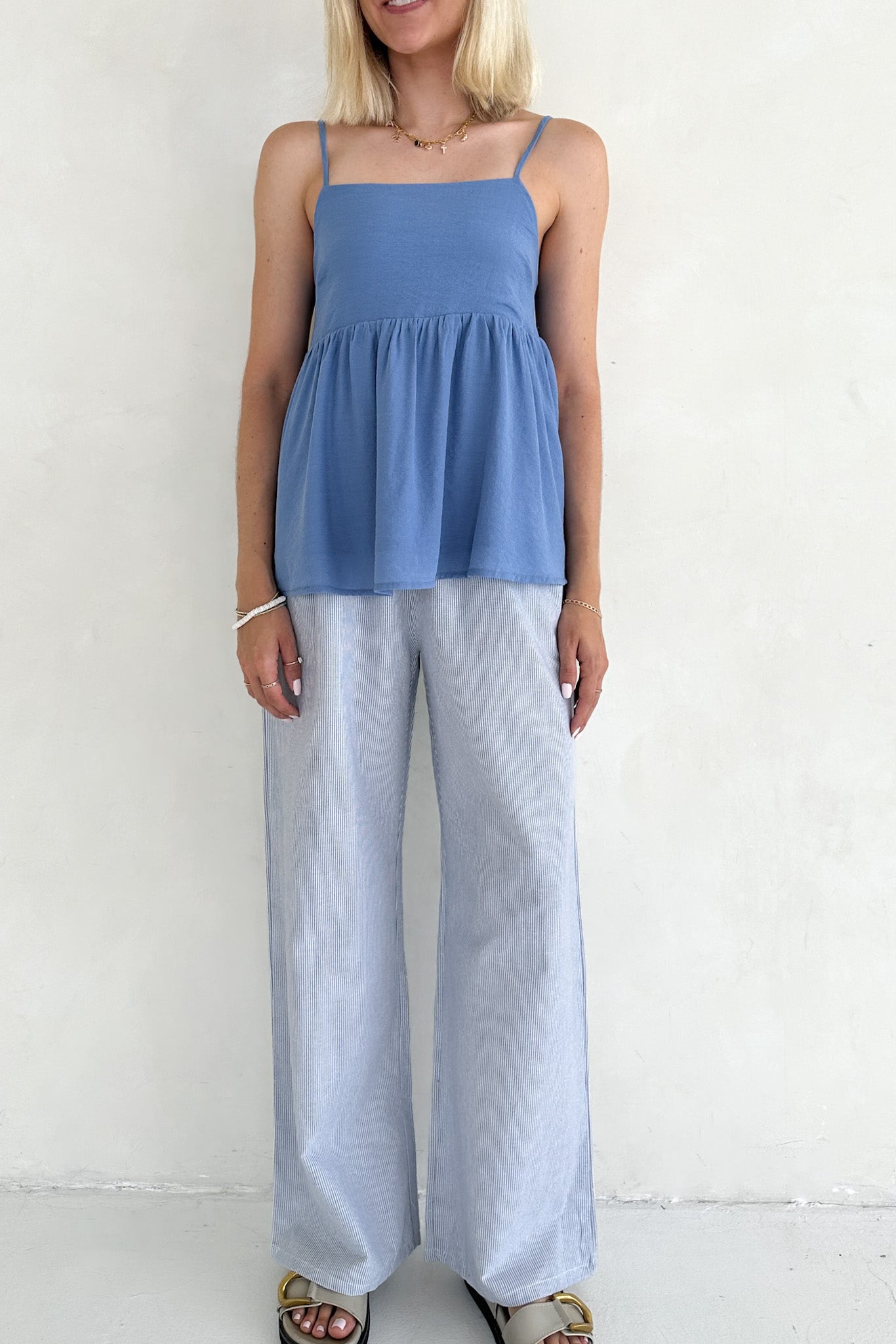 Woman wearing a blue top and light gray pants against a white background