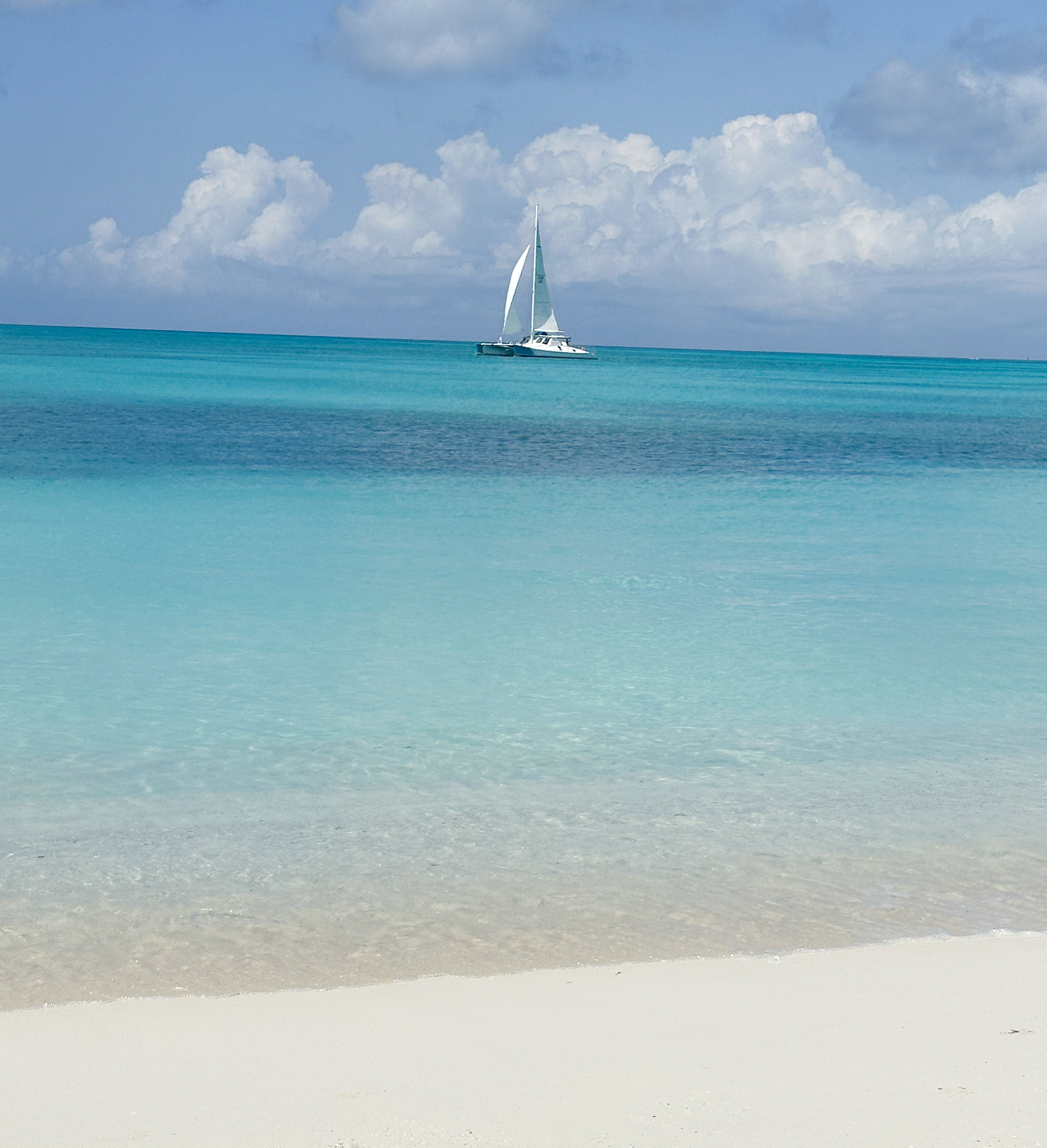 Sailboat on clear blue water with white sand and sky in the background