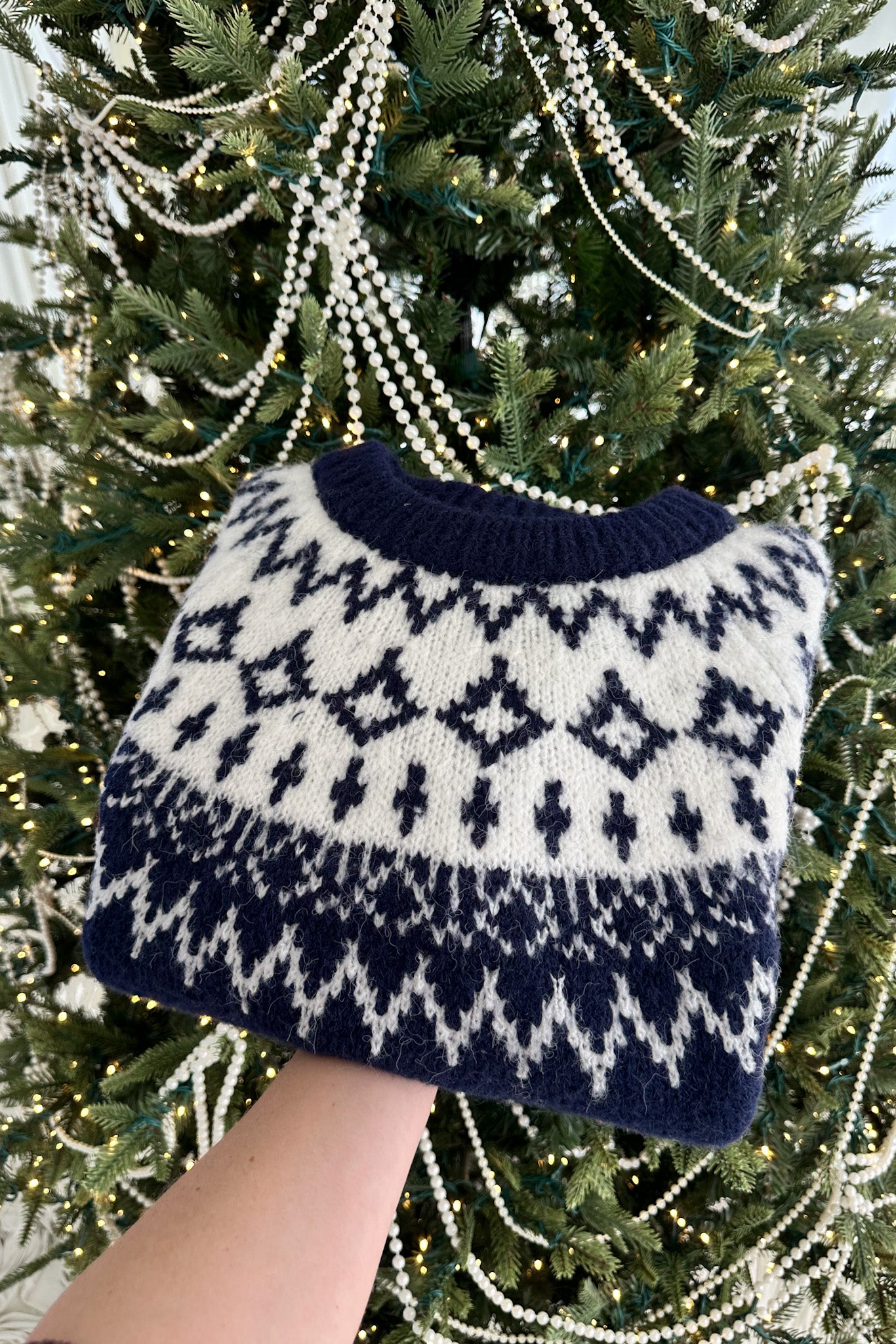 Navy and white patterned sweater held in front of a decorated Christmas tree.