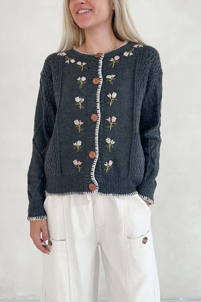 Person wearing a dark blue cardigan with floral embroidery on a plain background