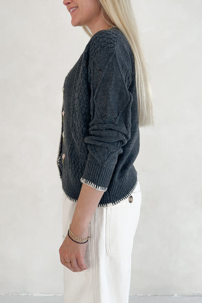 Person wearing a dark blue knitted sweater with white pants on a plain background