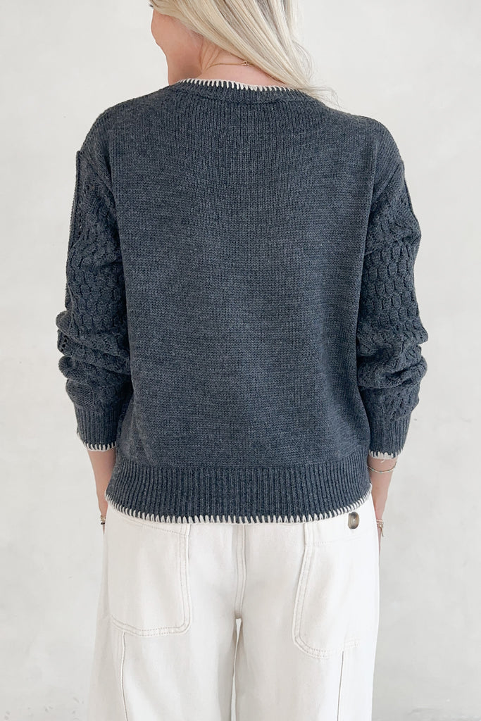 Person wearing a dark blue knitted sweater with white pants on a plain background