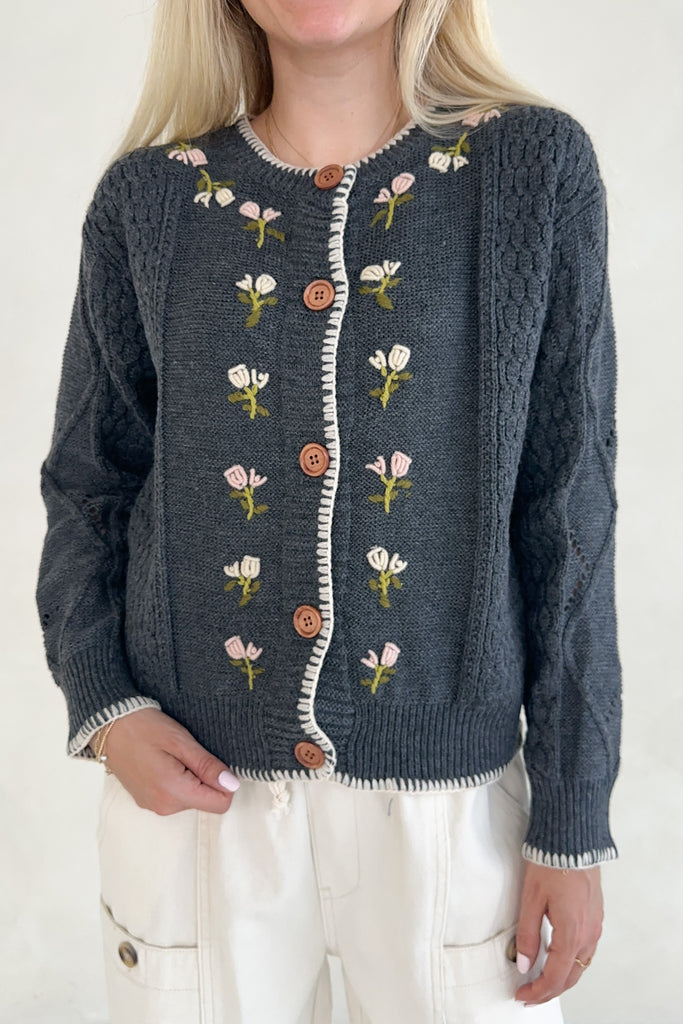 Person wearing a blue knitted cardigan with floral patterns and brown buttons on a white background