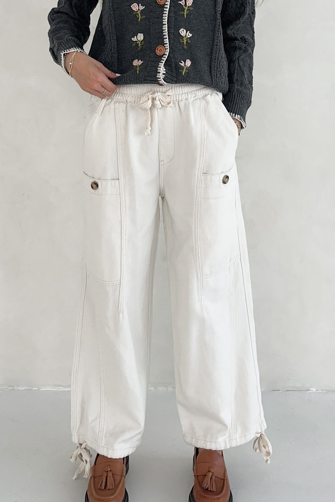 Person wearing white pants with a floral sweater and brown shoes on a plain background