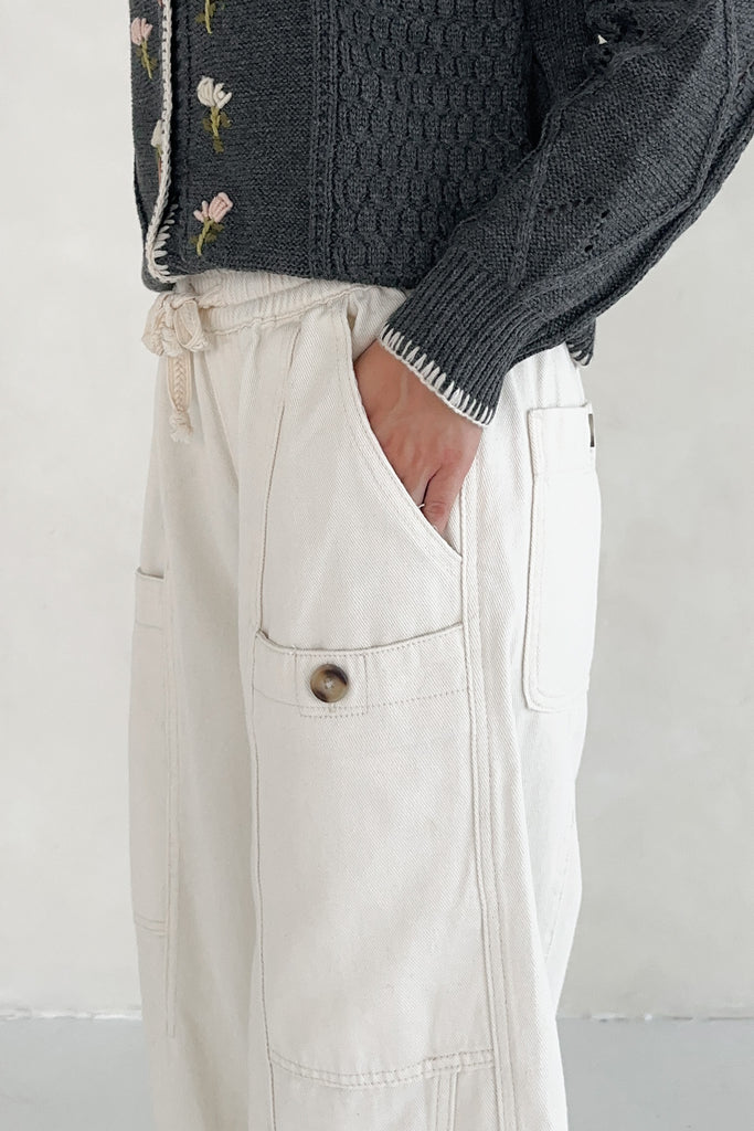 Person wearing a dark textured sweater and light-colored pants with a pocket on a plain background