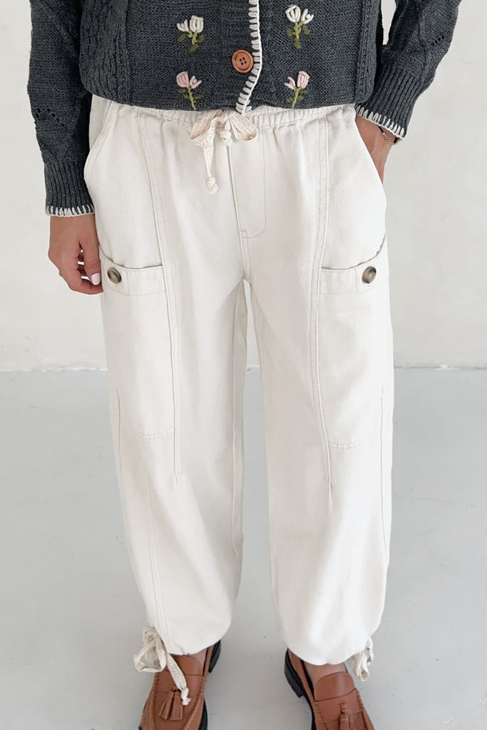 Person wearing white pants with a drawstring and button details, paired with a dark textured cardigan.