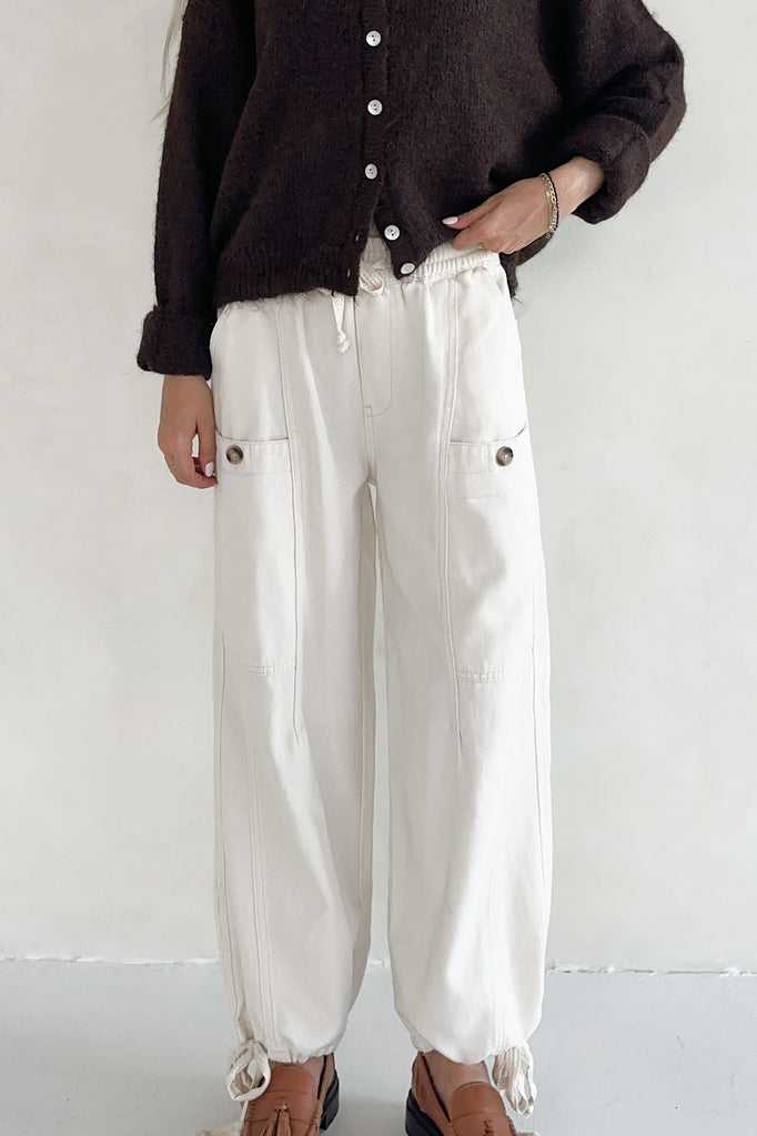 Person wearing a dark brown cardigan and white pants on a plain background