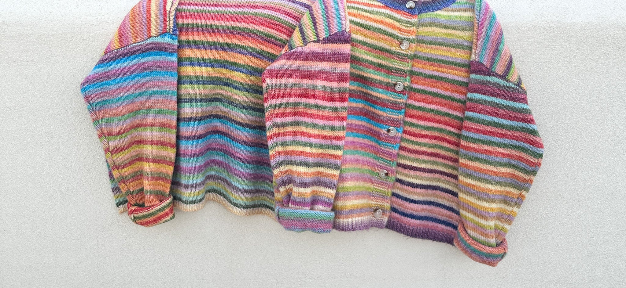 Multicolored striped cardigan on a white surface with greenery in the background
