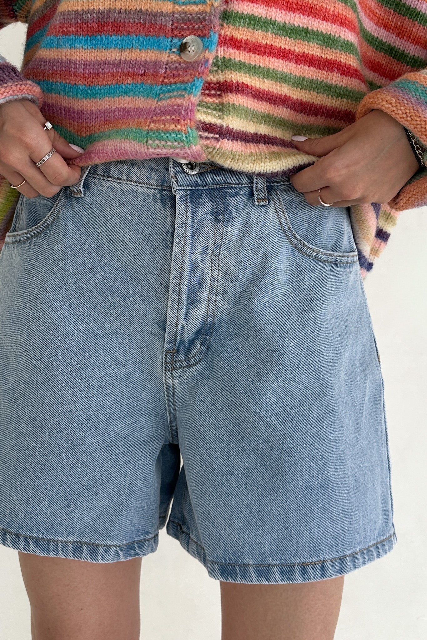 Person wearing a colorful striped sweater and blue denim shorts on a plain background