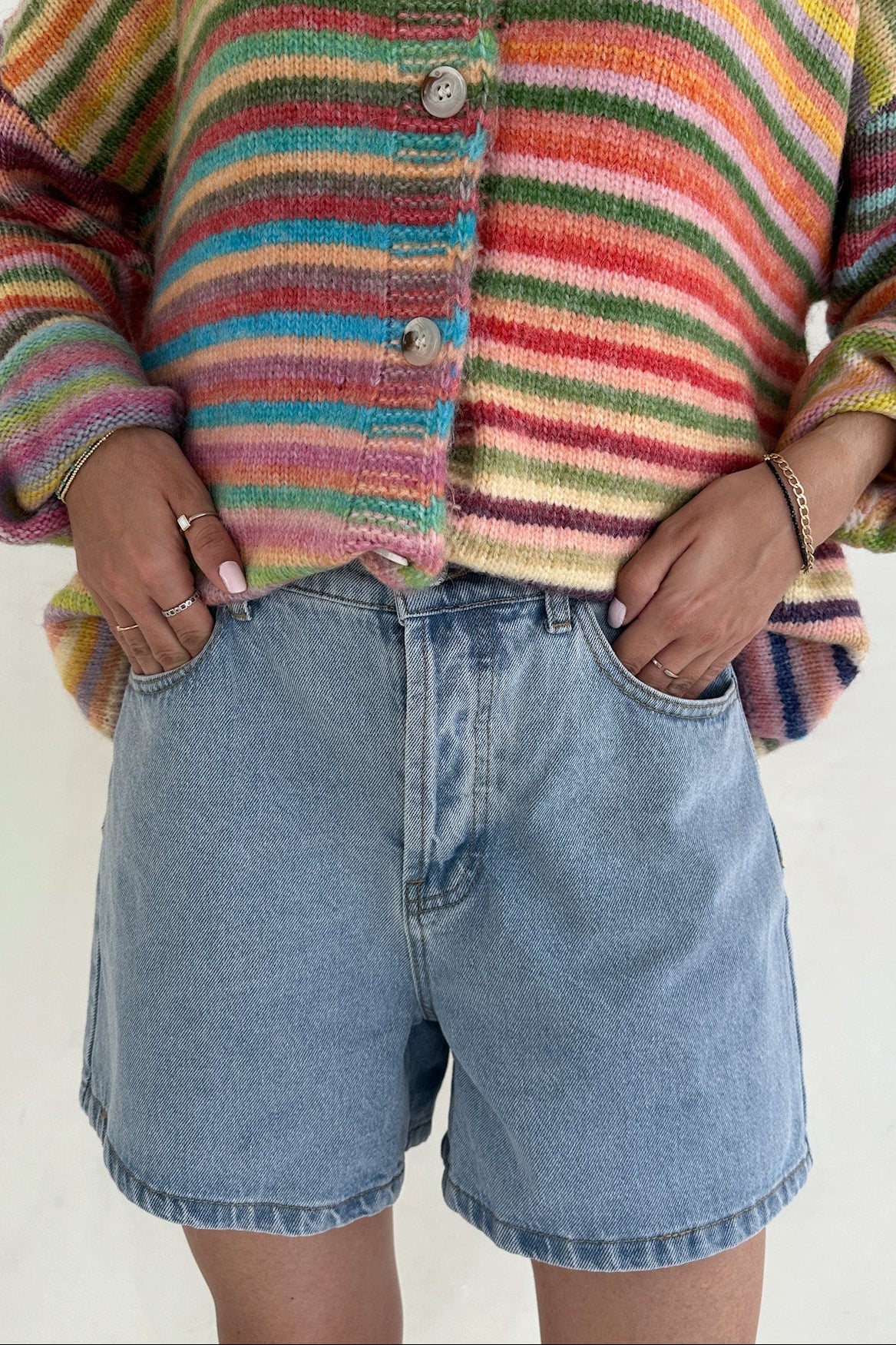 Person wearing a colorful striped sweater and denim shorts on a plain background
