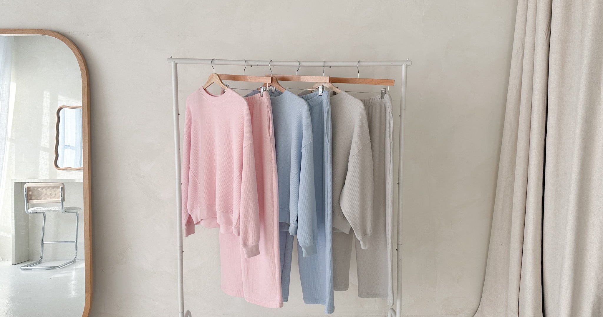 Clothing rack with pastel-colored sweaters in a minimalistic room.