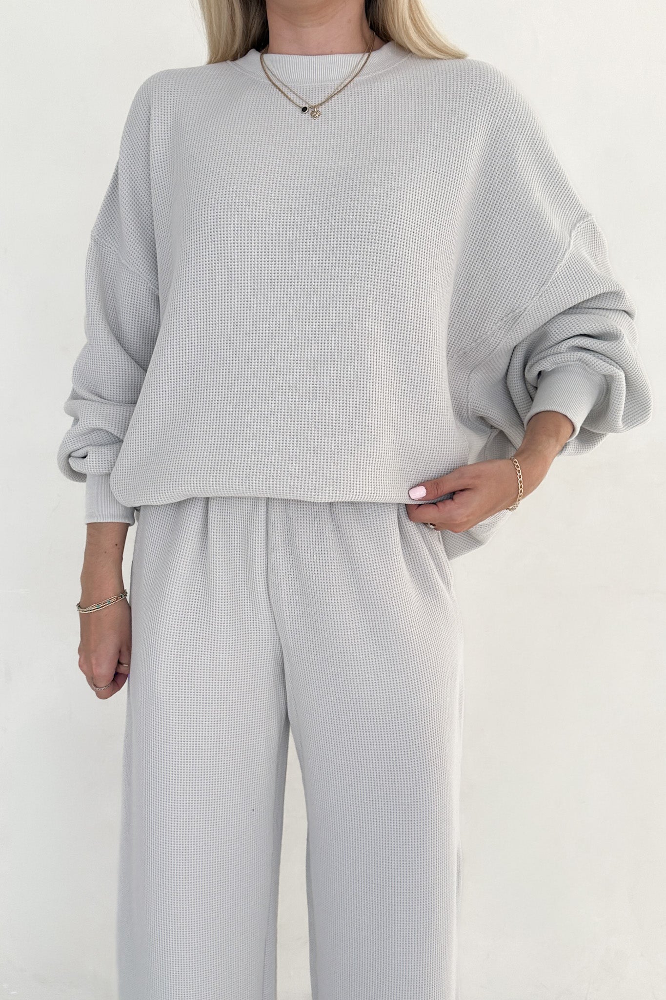 Person wearing a light gray sweater and pants on a white background