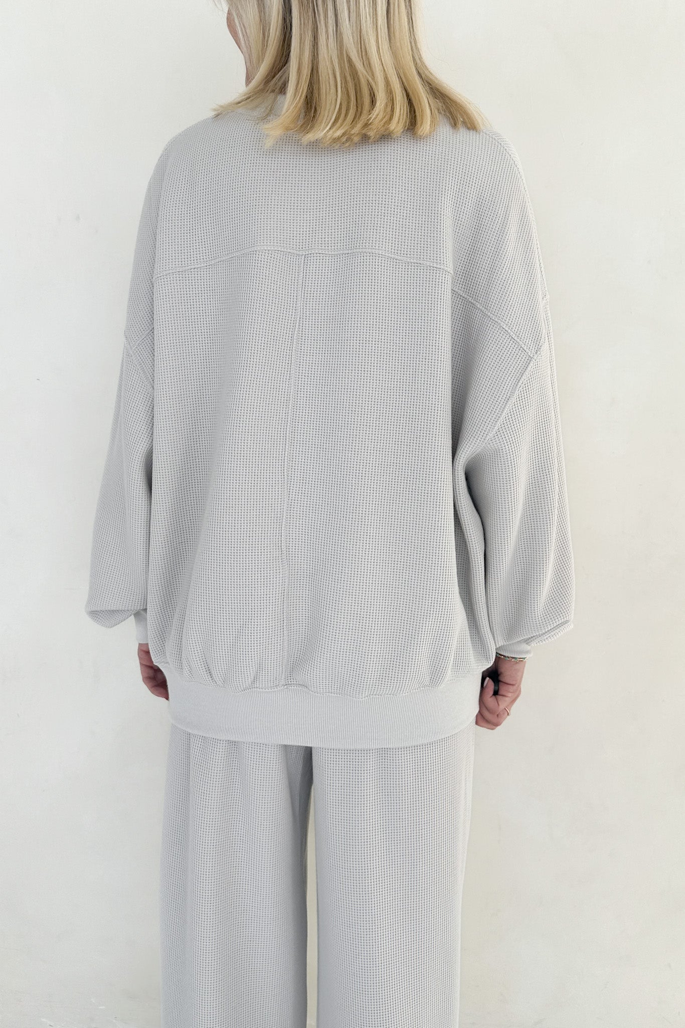 Person wearing a light gray oversized sweater and pants on a white background