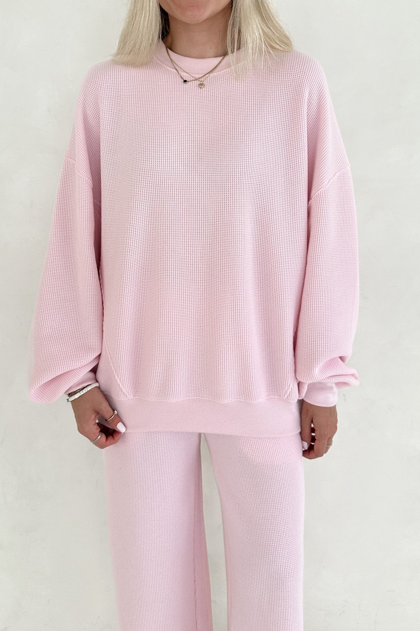 Person wearing a pink ribbed sweater and pants on a white background