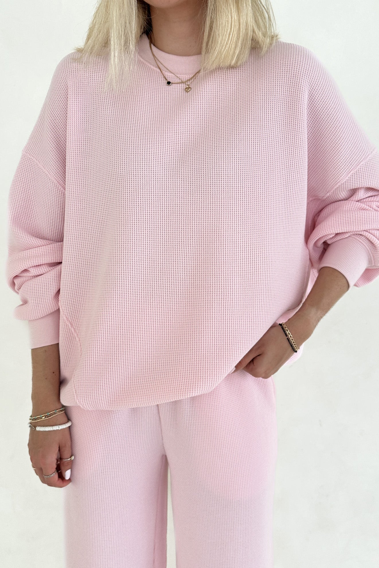 Person wearing a pink textured sweater and pants on a white background
