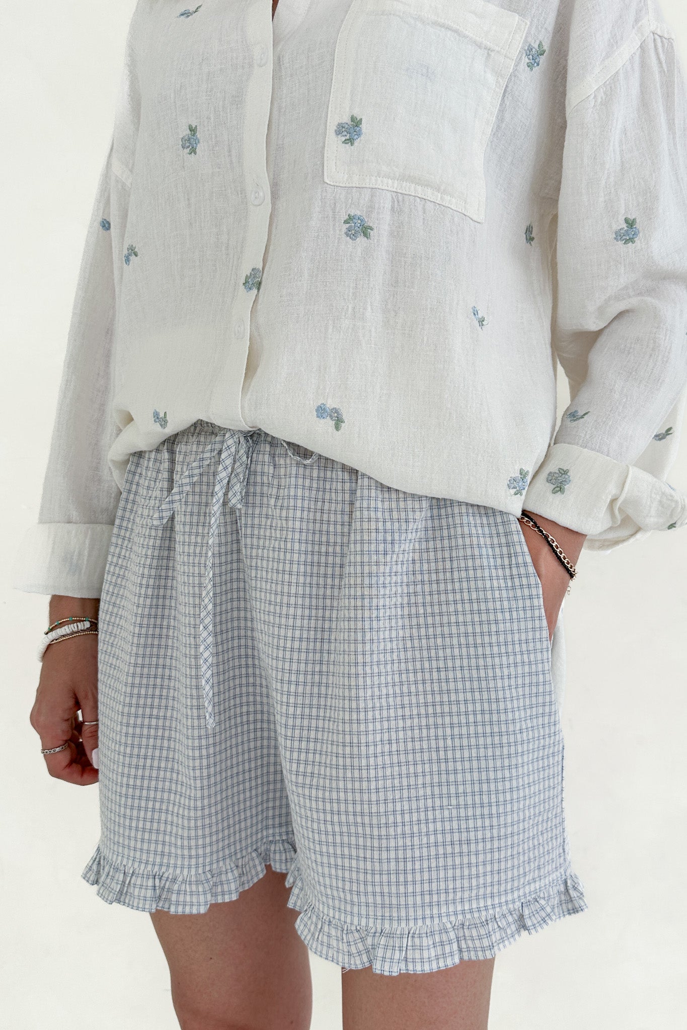 Person wearing a white embroidered shirt and checkered shorts on a plain background