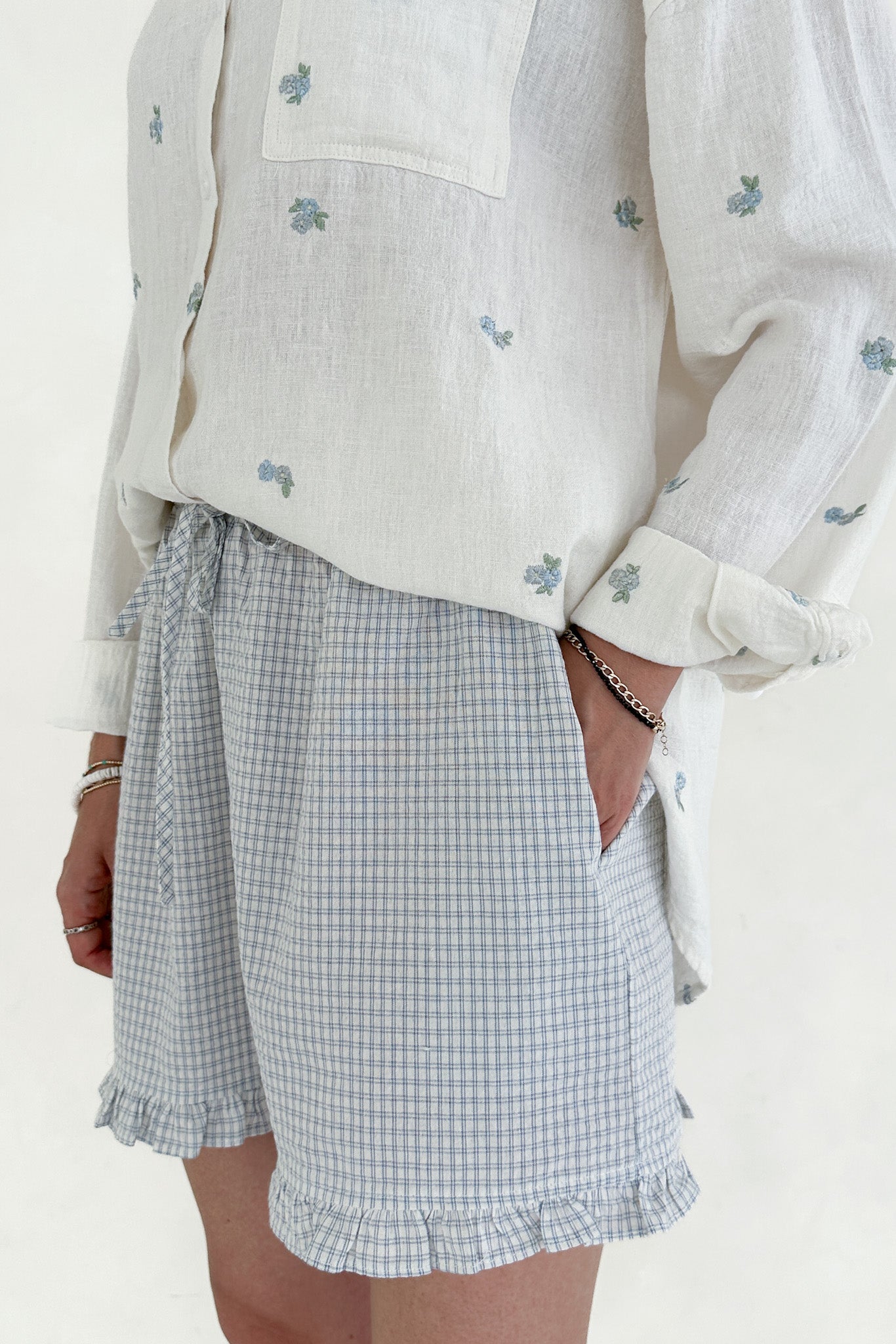 Person wearing a light-colored embroidered shirt and a checkered skirt on a white background