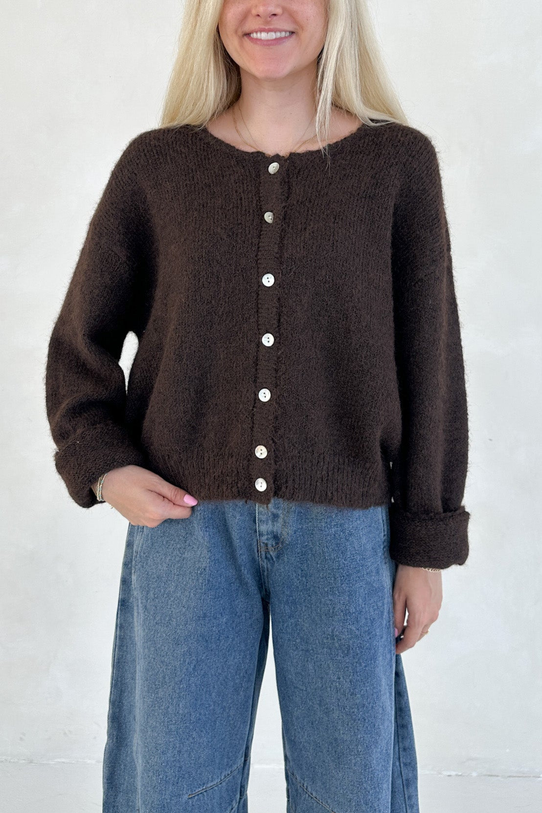 Woman wearing a brown cardigan with white buttons and blue jeans against a white background