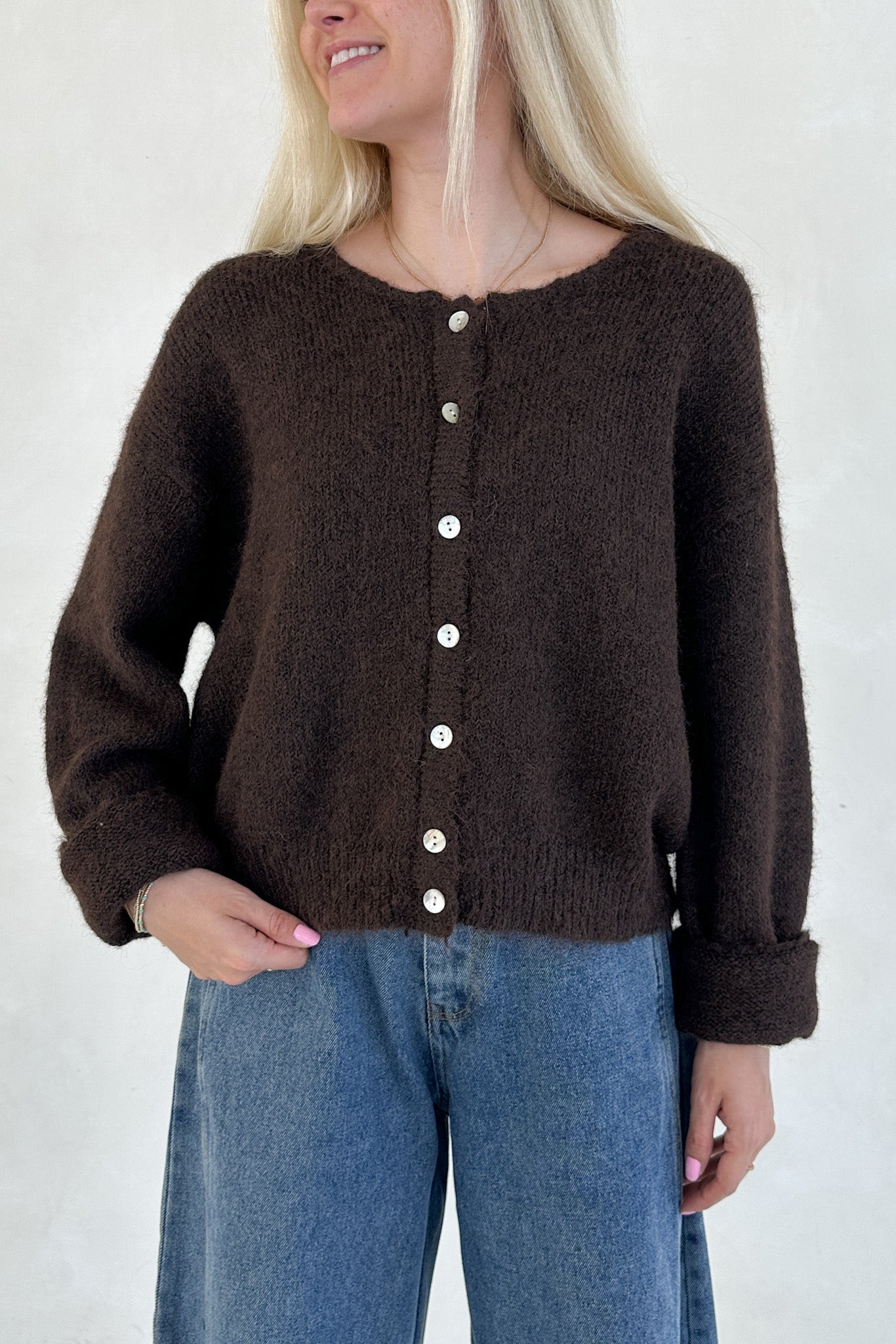 Person wearing a brown knitted cardigan with white buttons against a plain background