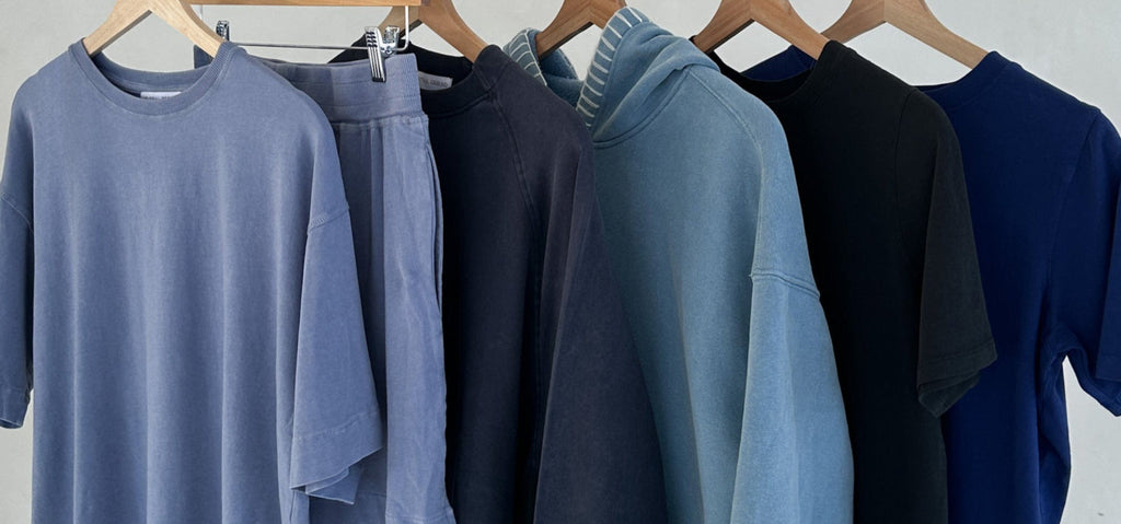 Collection of shirts and pants in various shades of blue and black on hangers against a light gray background.