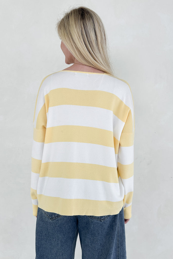 Person wearing a yellow and white striped sweater with blue jeans on a plain background