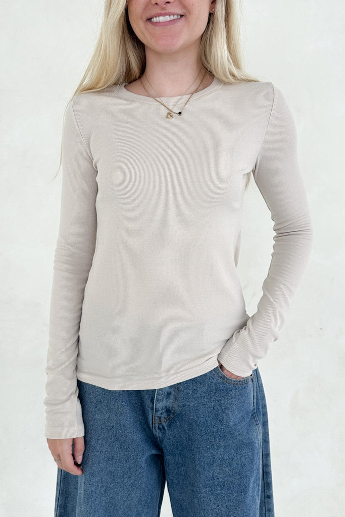 Woman wearing a beige long-sleeve top and blue jeans against a white background