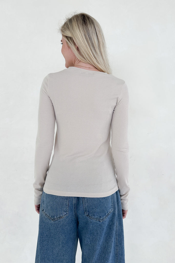 Person wearing a beige long-sleeve top and blue jeans on a white background