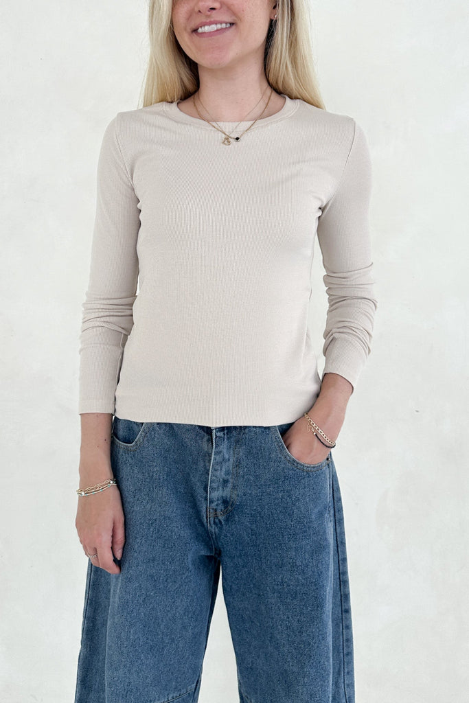 Person wearing a beige long-sleeve top and blue jeans against a white background
