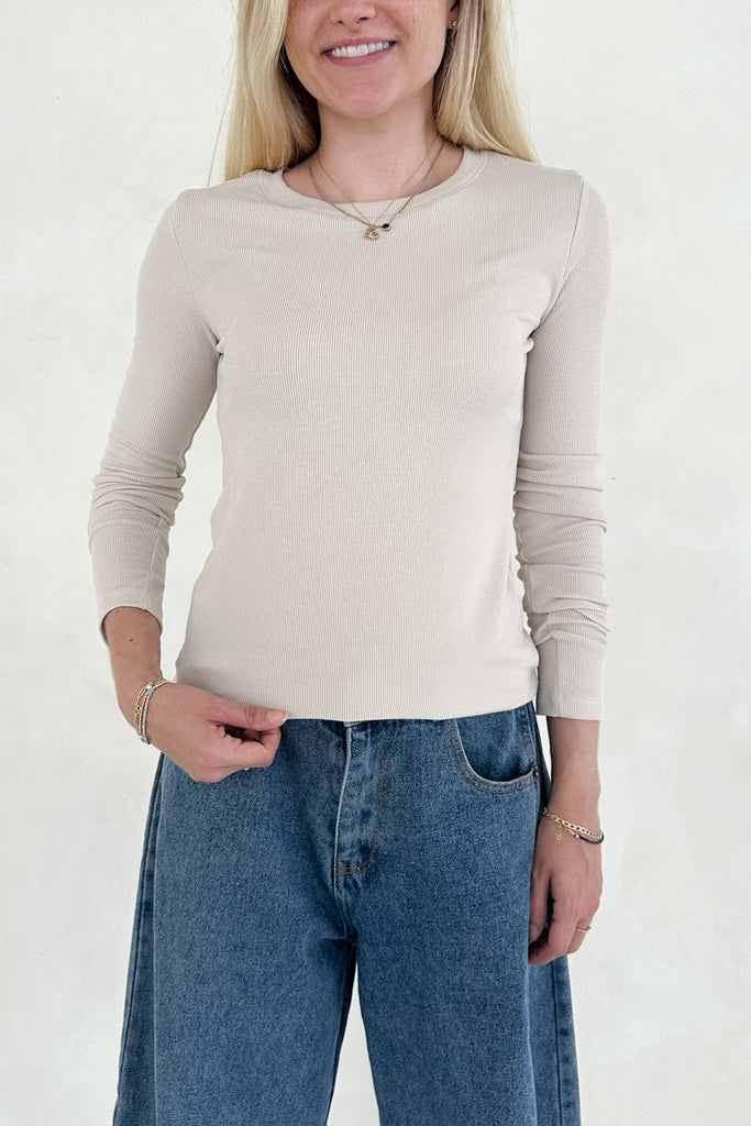 Woman wearing a beige long-sleeve top and blue jeans against a white background