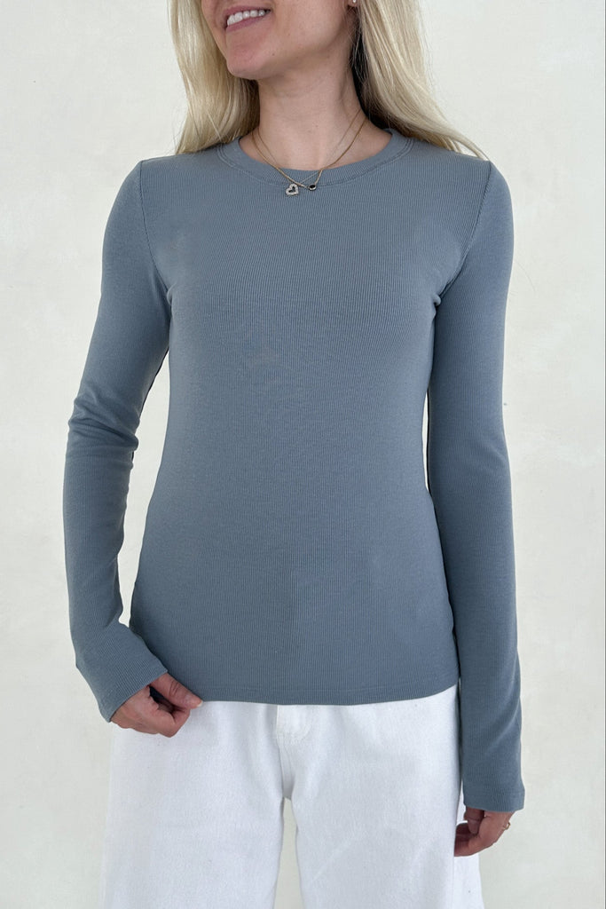 Woman wearing a blue long-sleeve top and white pants against a plain background