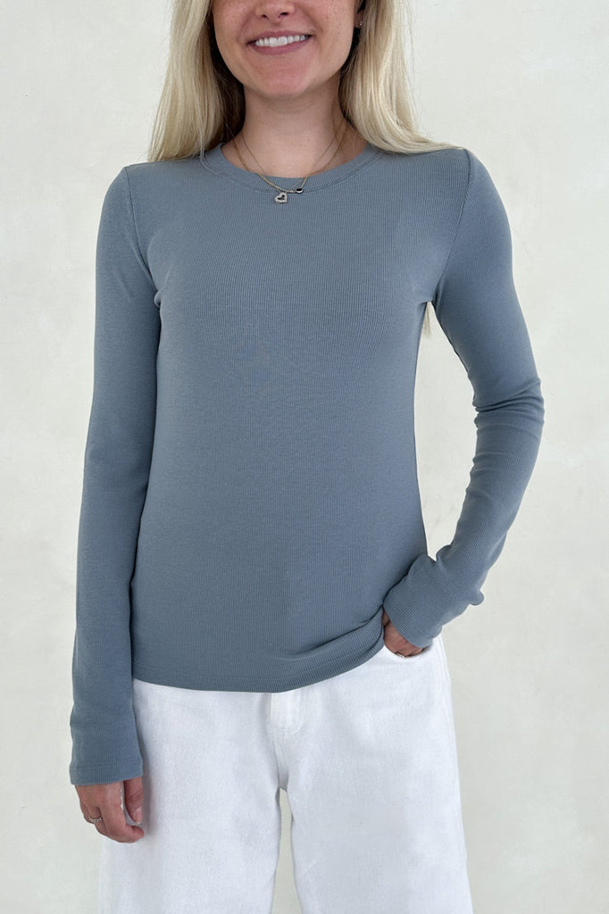 Woman wearing a blue long-sleeve top and white pants against a plain background