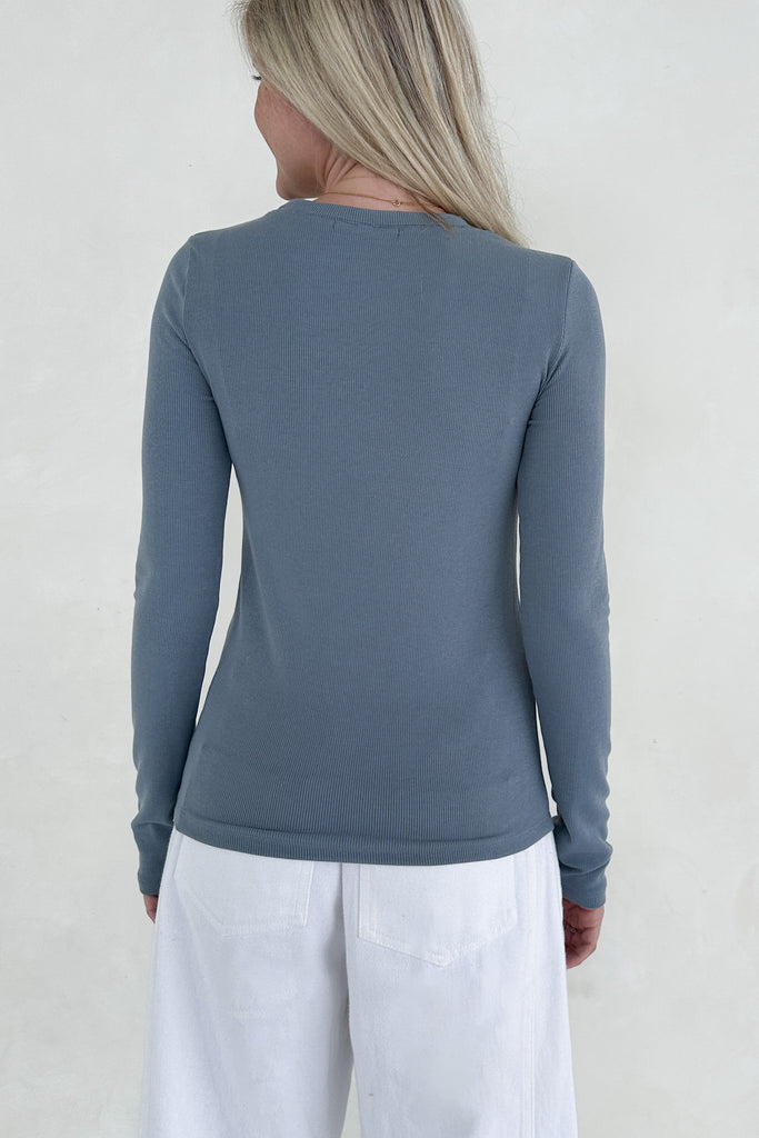 Person wearing a blue long-sleeve top and white pants against a plain background
