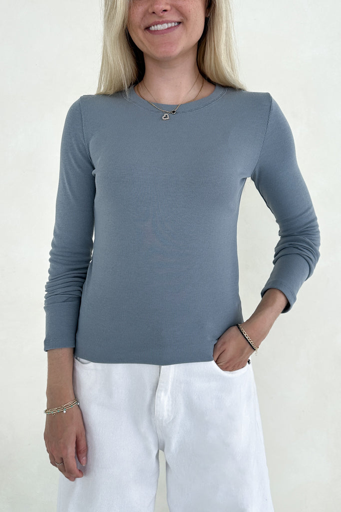 Woman wearing a blue long-sleeve top and white pants against a plain background