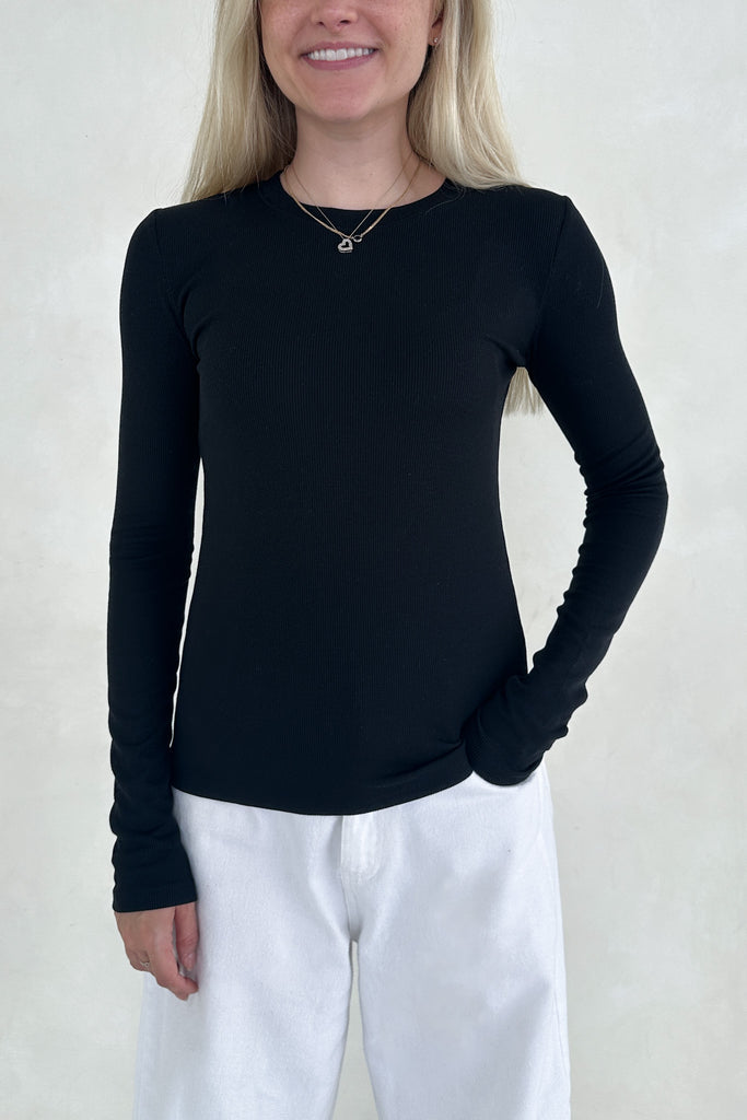 Person wearing a black long-sleeve top and white pants against a plain background