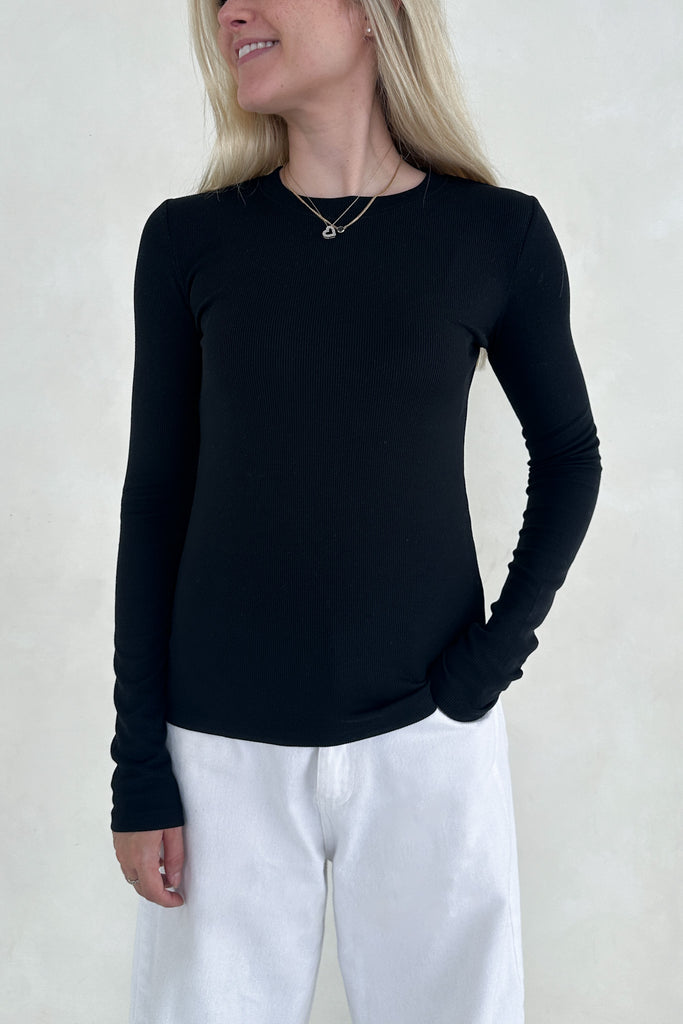 Person wearing a black long-sleeve top and white pants against a plain background