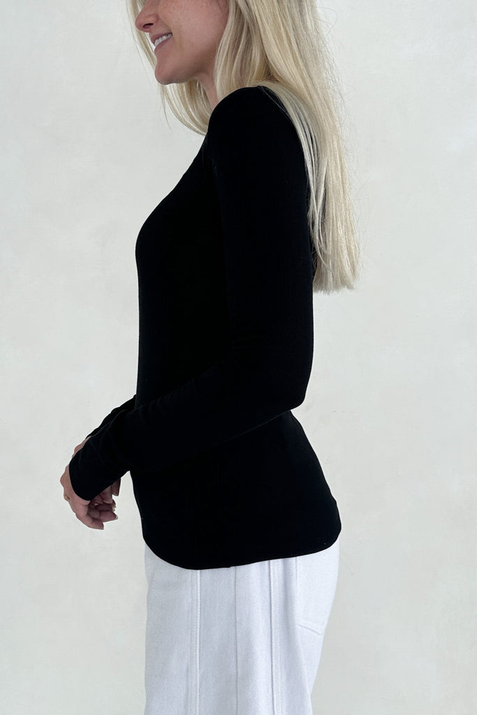 Woman wearing a black blazer and white pants on a plain background