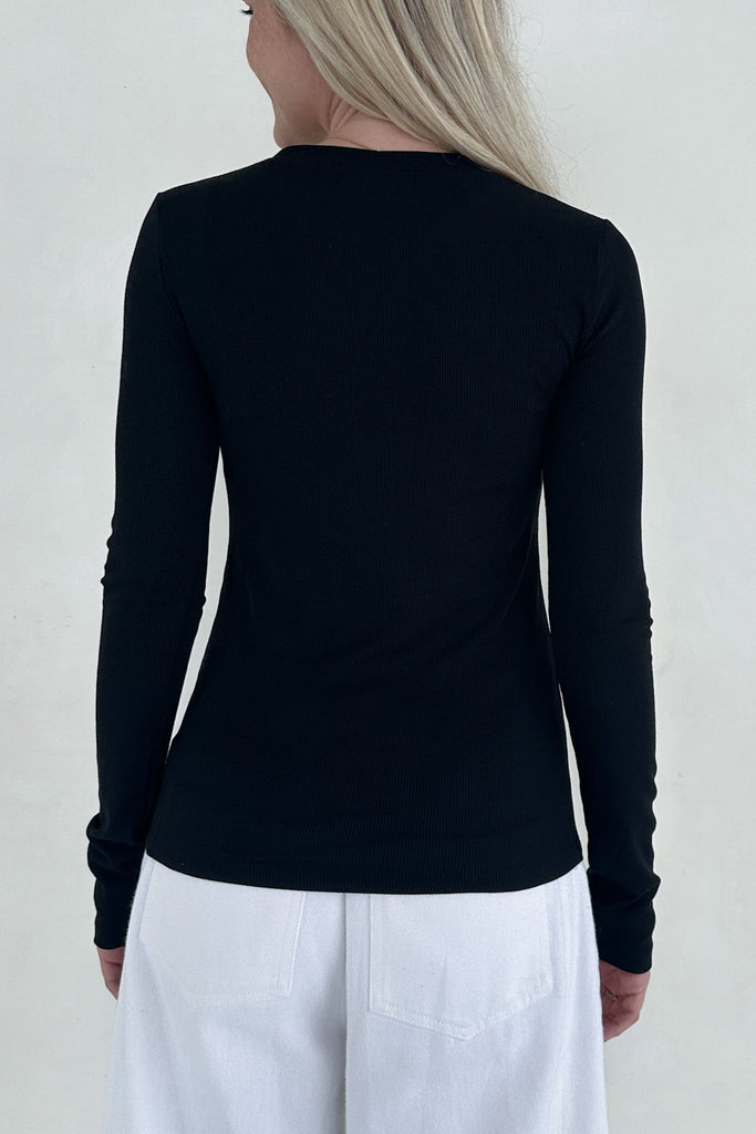 Person wearing a black long-sleeve top and white pants against a plain background